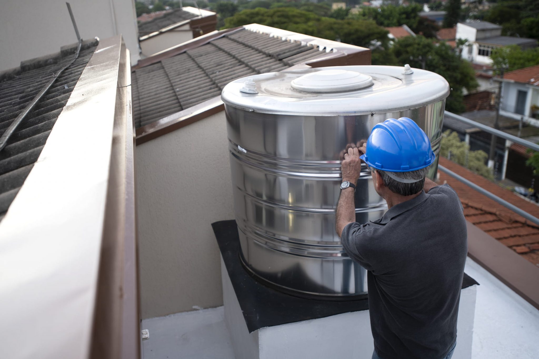 Homem mexendo em caixa d'agua de aço inoxidável em cima de telhado de casa