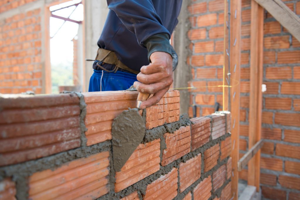 Homem construindo uma parede com tijolos e cimento