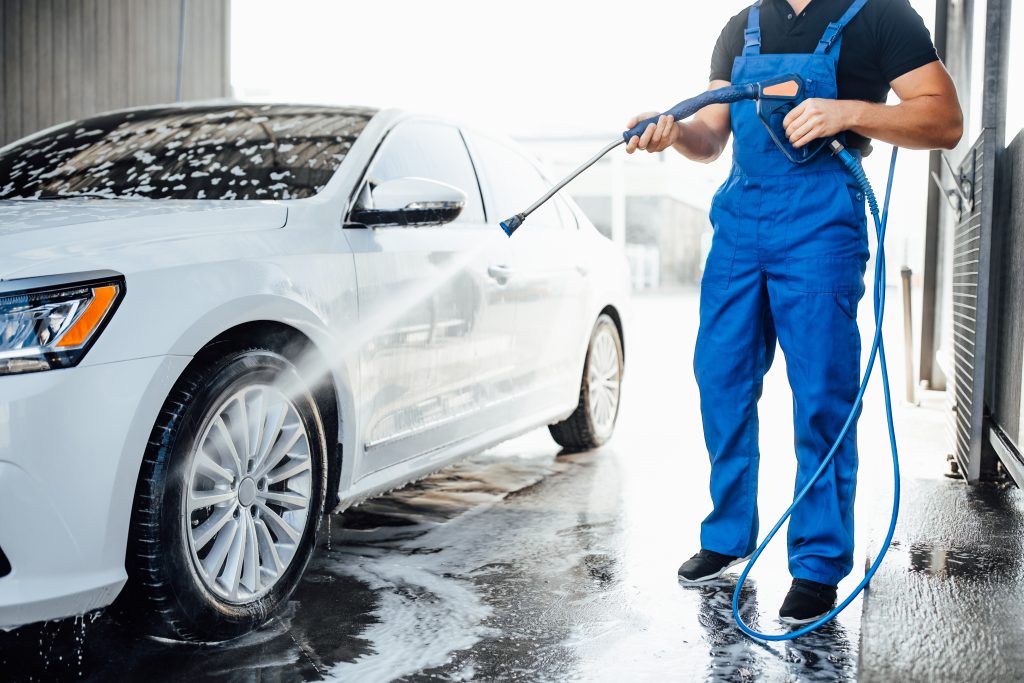 Homem lavando carro com uma mangueira com alta pressão