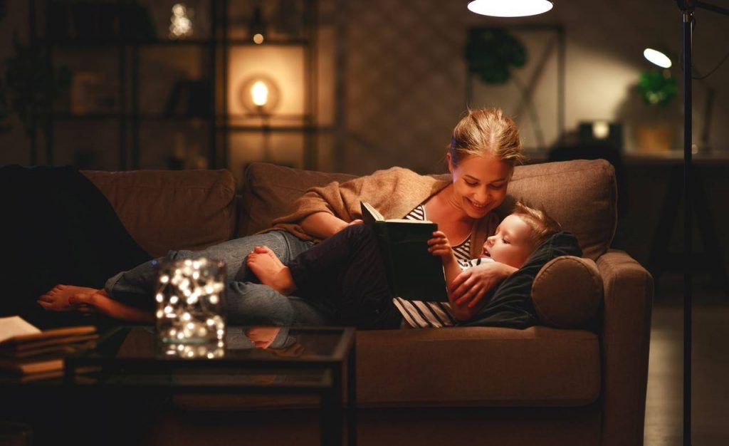 Mãe e filho deitados no sofá lendo um livro