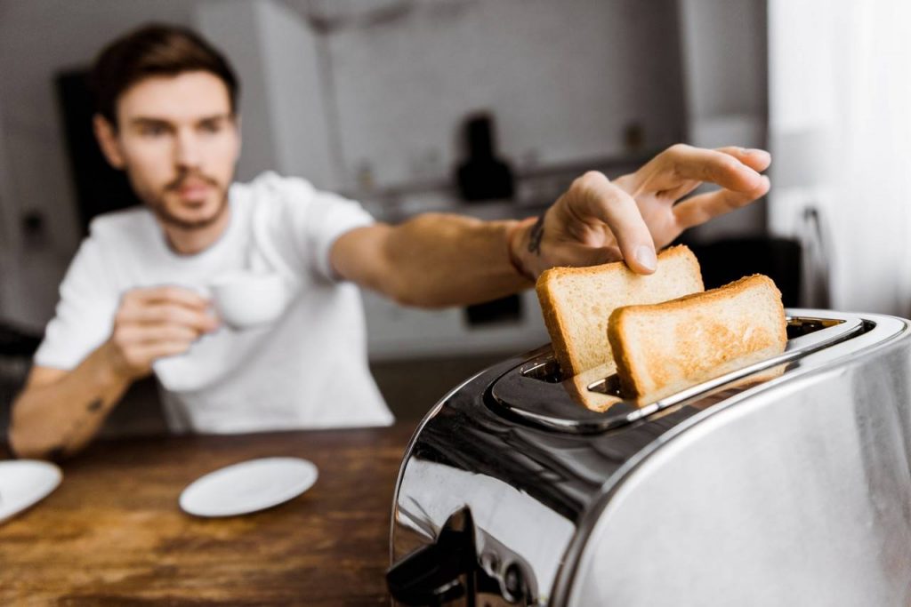 Homem pegando o pão que estava sendo torrado na torradeira