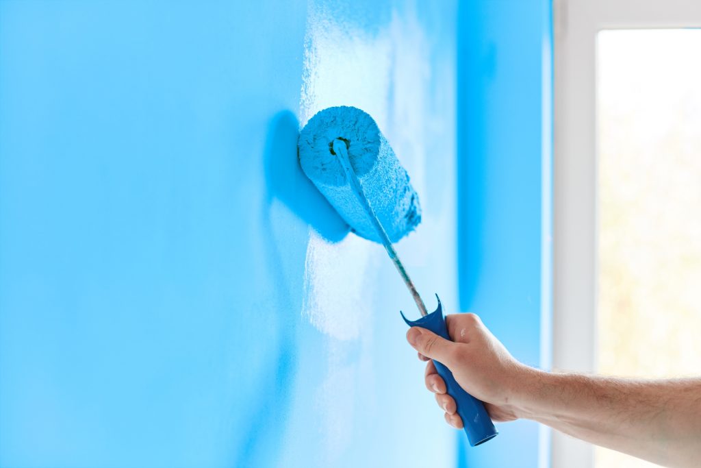 rolo de tinta deslizando a cor azul pela parede, escolher a tinta ideal para superfície