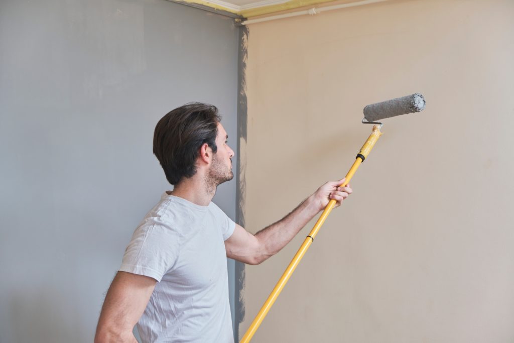 homem pintando a parede de com cômodo da casa com um rolo de pintura e um extensor