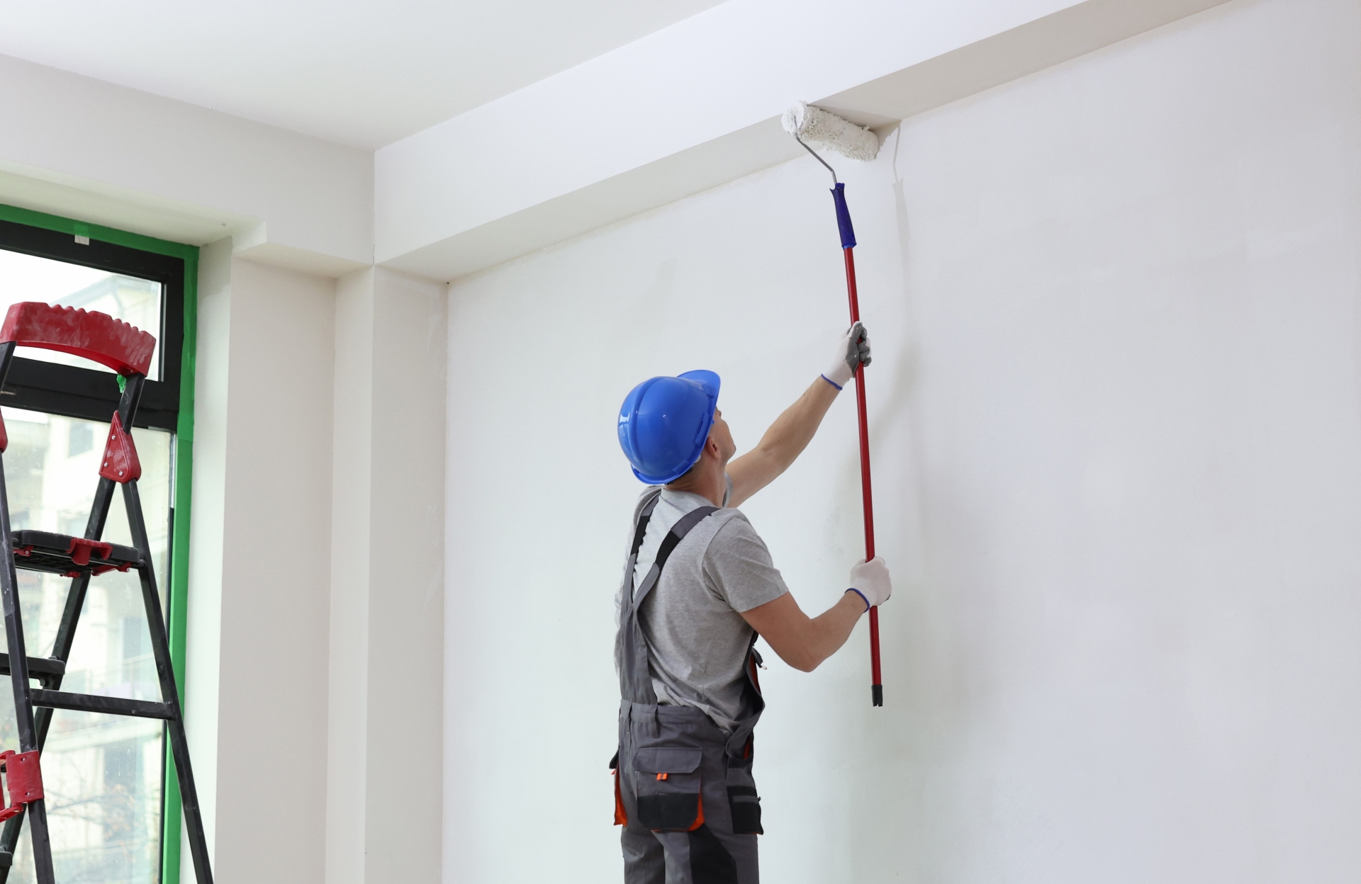 pintor deslizando rolo de pintura na parede com produto fazendo a preparação da superfície para pintura