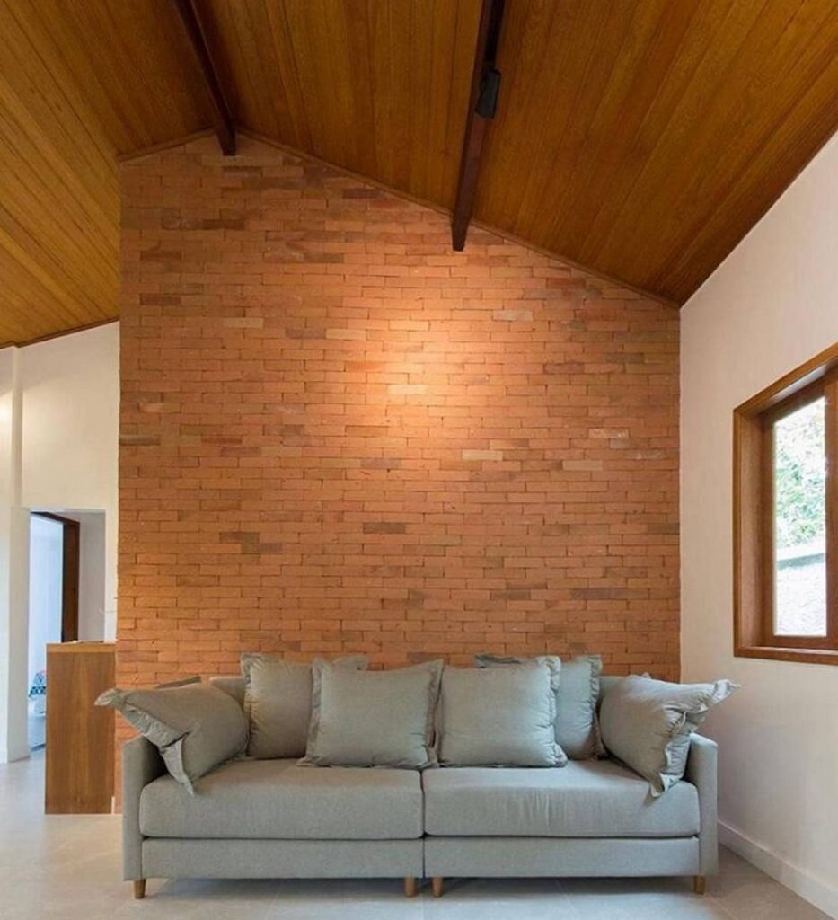 Sala de estar com sofá cinza e parede com tijolinho rústico é um dos revestimentos que imitam materiais naturais
