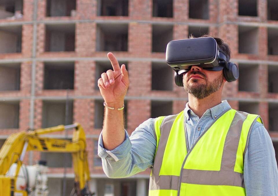 Homem utilizando EPI's com óculos de realidade virtual, ao fundo construção de prédio