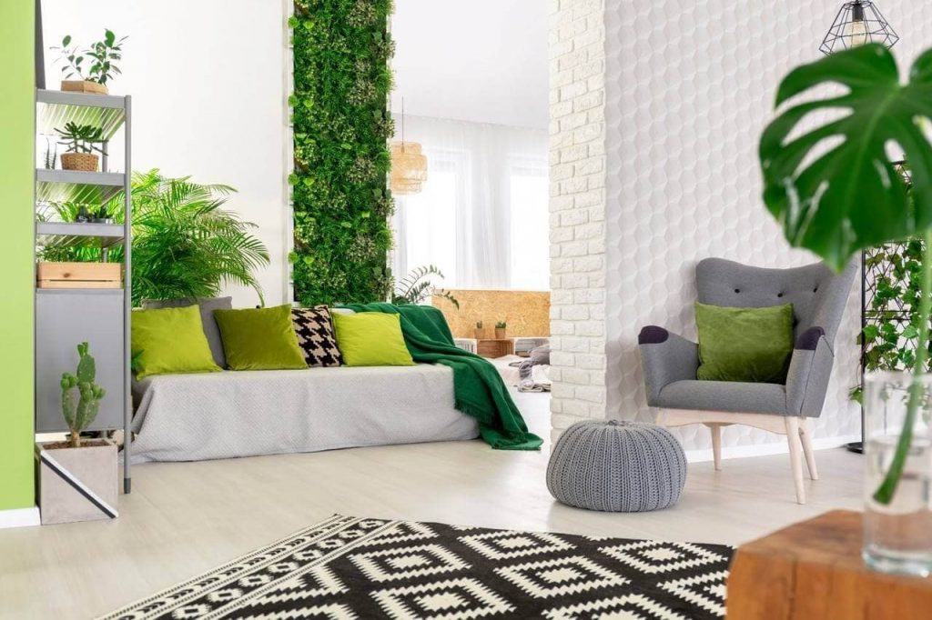 Sala decorada com poltrona, sofá com almofadas, tapete, vaso de plantas, e ao fundo jardim vertical