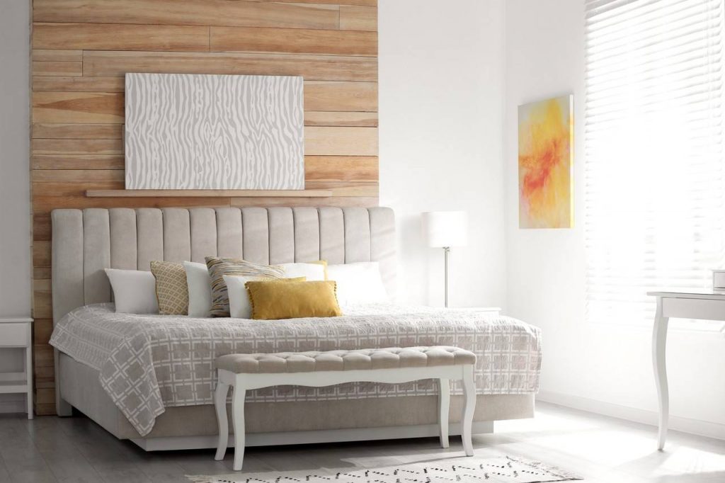 Dormitório de paredes branca, com parte decorativa com estampa de madeira, quadros decorativos, cama de casal e recamier ao pé