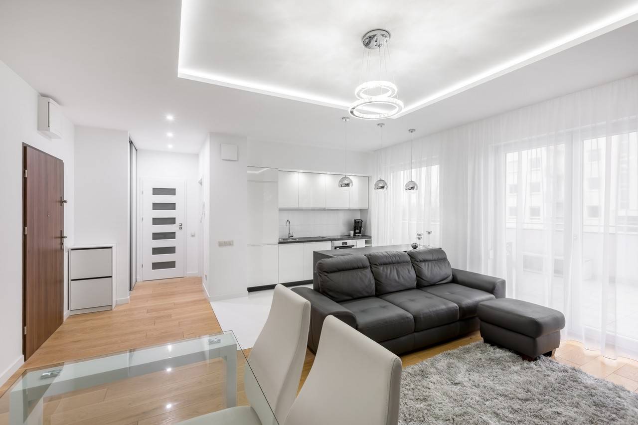 sala e cozinha de conceito aberto, sofá de couro no tom preto, tapete cinza, mesa de jantar de vidro com cadeiras brancas