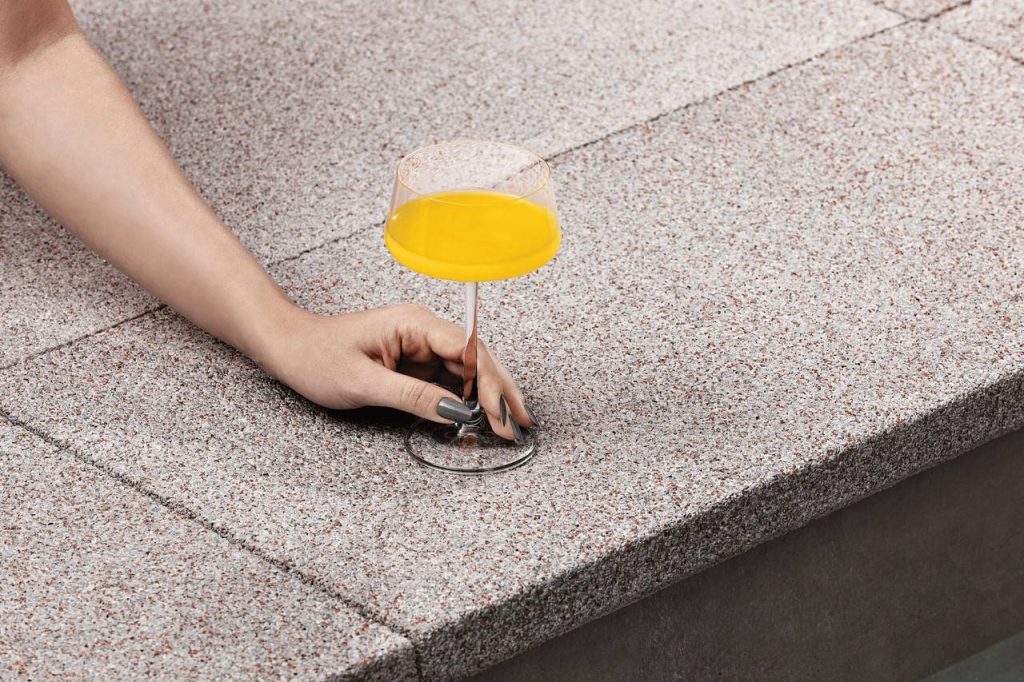 taça de vidro com bebida na cor laranjada, com pessoa colocando no chão com piso fulget 