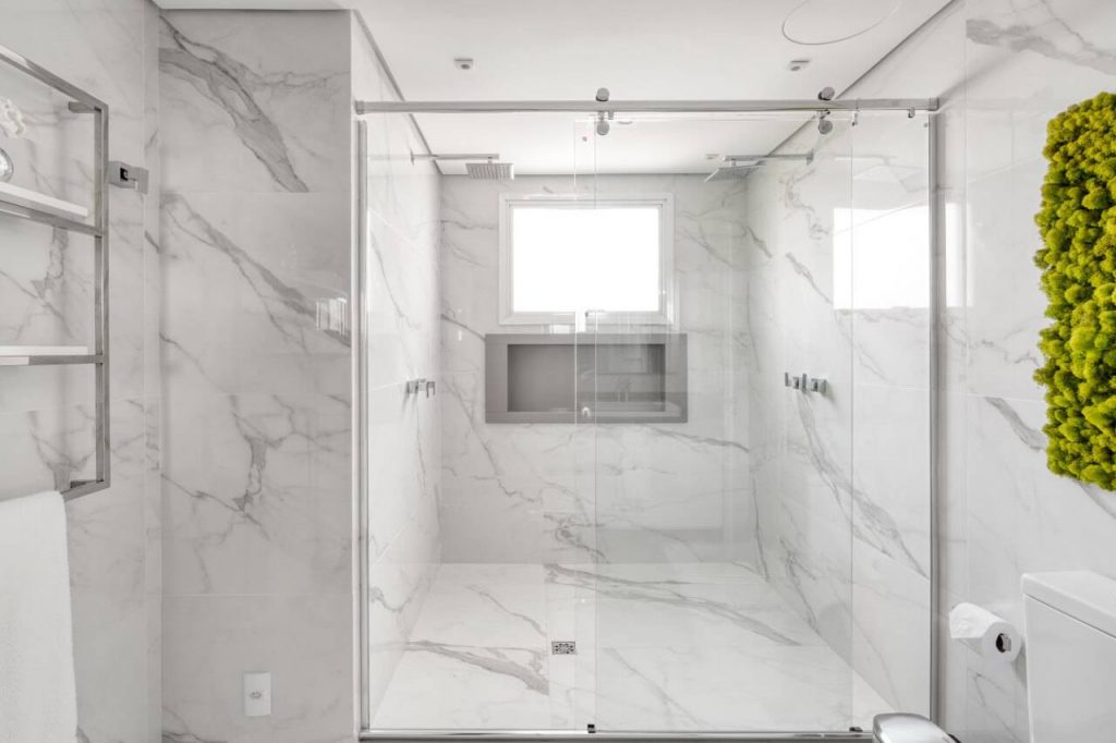 Revestimento de parede de banheiro em porcelanato marmorizado, box de correr em vidro transparente