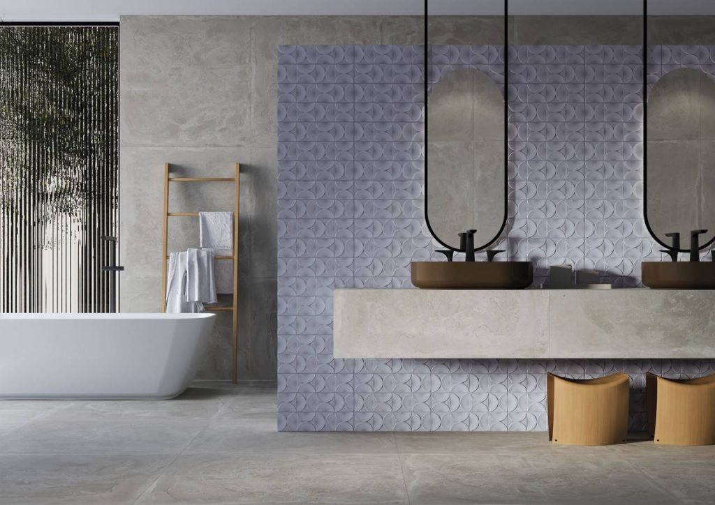 Revestimento de parede de banheiro em porcelanato com textura, dois espelhos fixos na parede, pia com duas cubas sobrepostas, banheira branca com prateleira de madeira