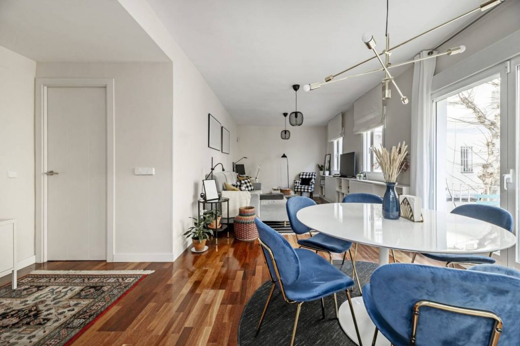 ambiente interno de conceito aberto, com mesa de jantar branca com cadeiras no tom azul, ao fundo sofá no tom claro e TV são tendências para arquitetura