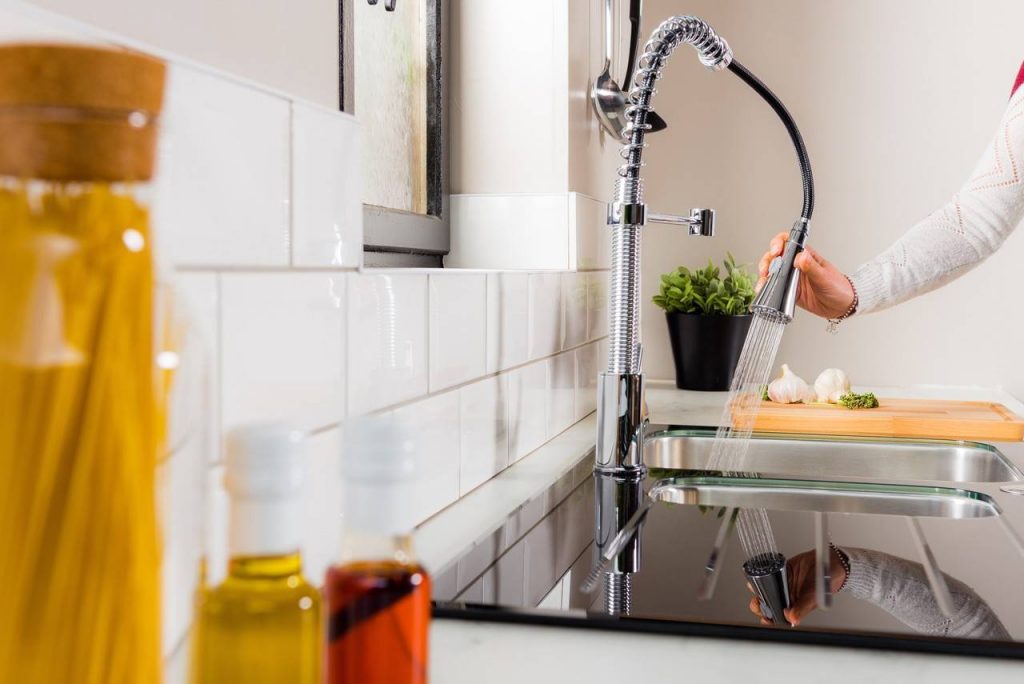 Torneira gourmet flexível ligada com pessoa jateando água na pia da cozinha