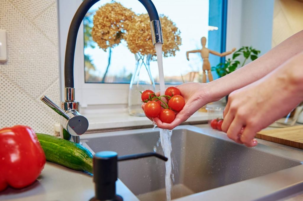 Torneira com misturador ligada com pessoa lavando tomates na pia da cozinha está entre os tipos de torneiras confortáveis