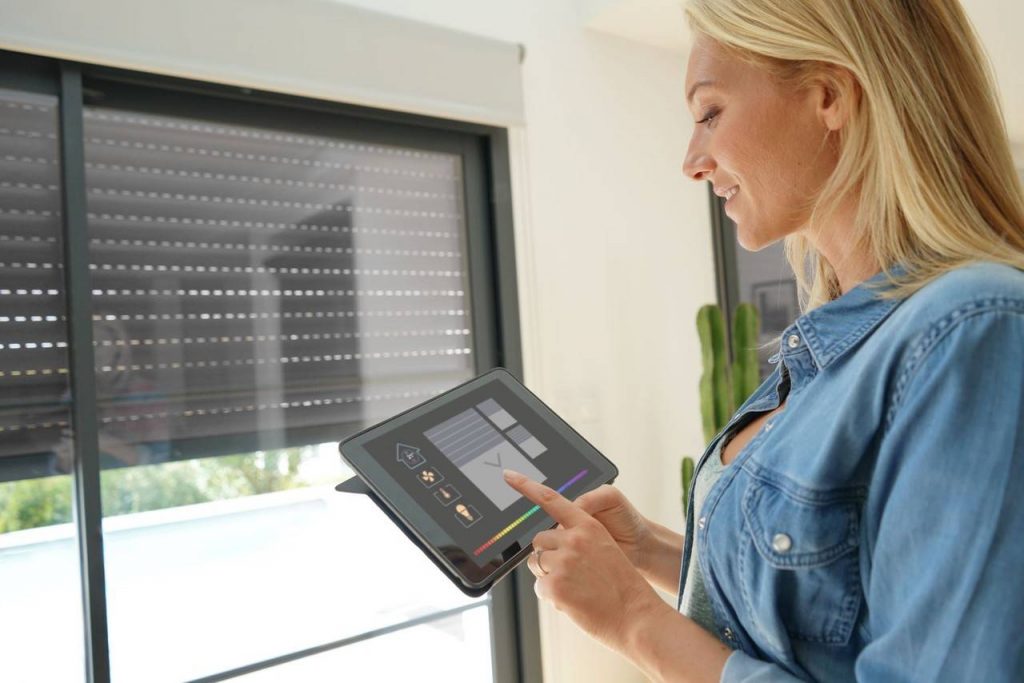 Mulher manuseando tablet com aplicativo de automação residencial controlando abertura de janela