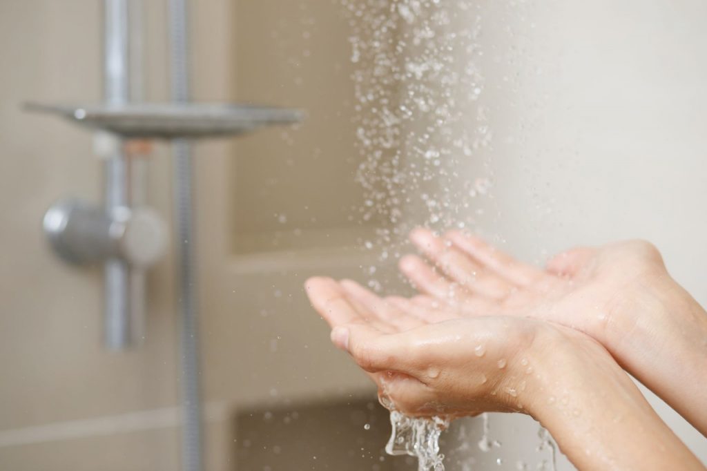 Pessoa formando uma concha com as duas mãos em baixo do chuveiro ligado
