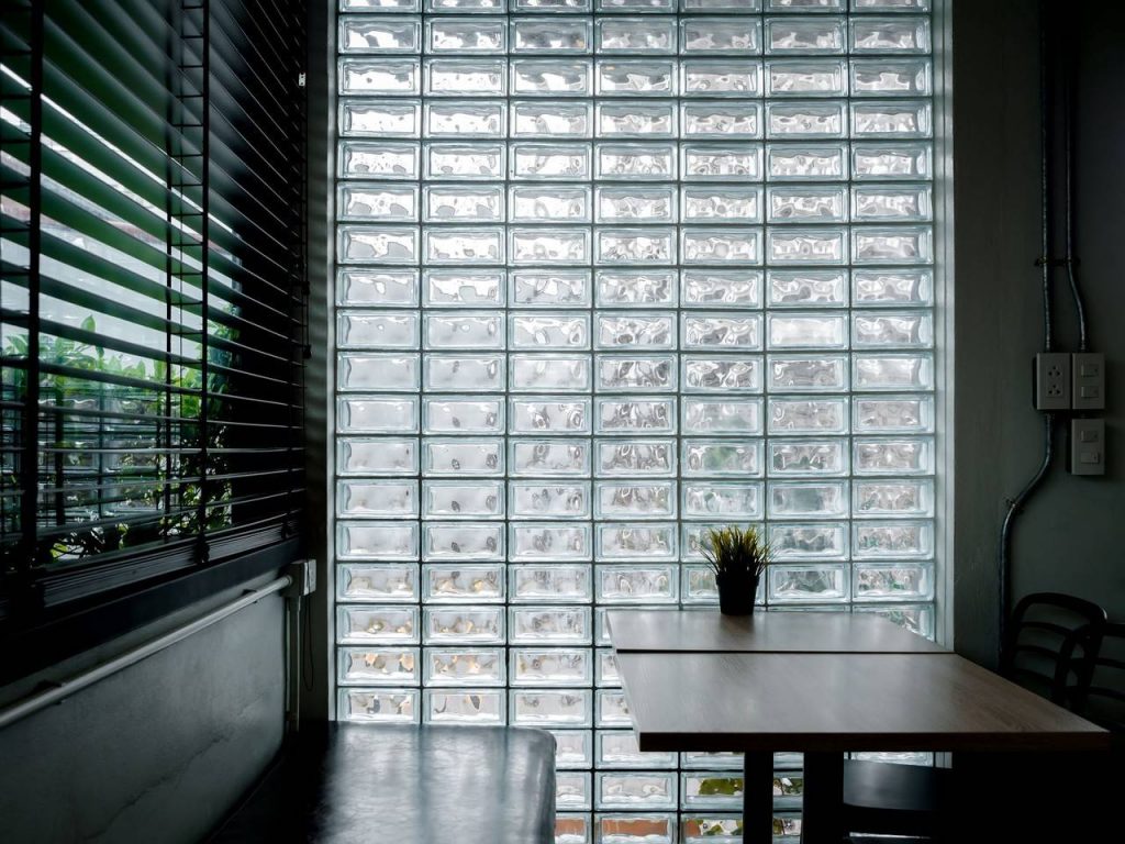 Tijolos de vidro da marca Vitraltec instalados em parede  de ambiente interno, com conjunto de mesa e cadeira