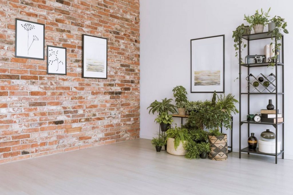 Parede de sala, decoradas com papel de parede simulando tijolos, quadros decorativos, estante com plantas e vasos