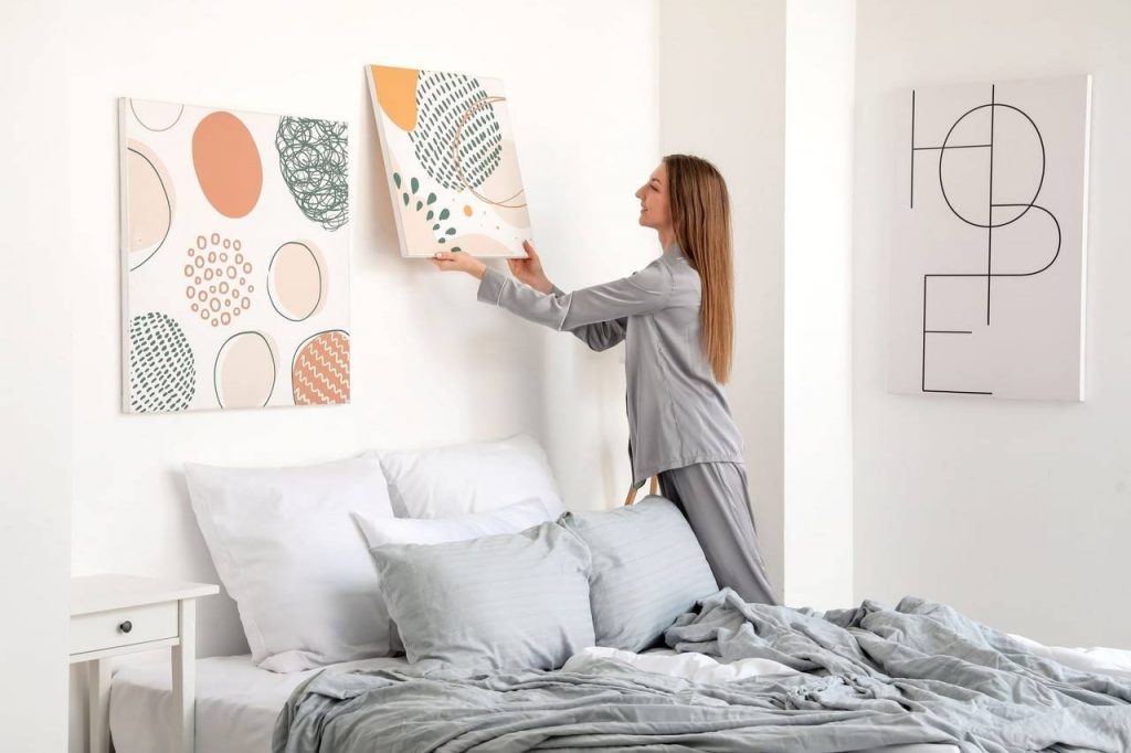 Mulher decorando paredes de dormitório com quadros 