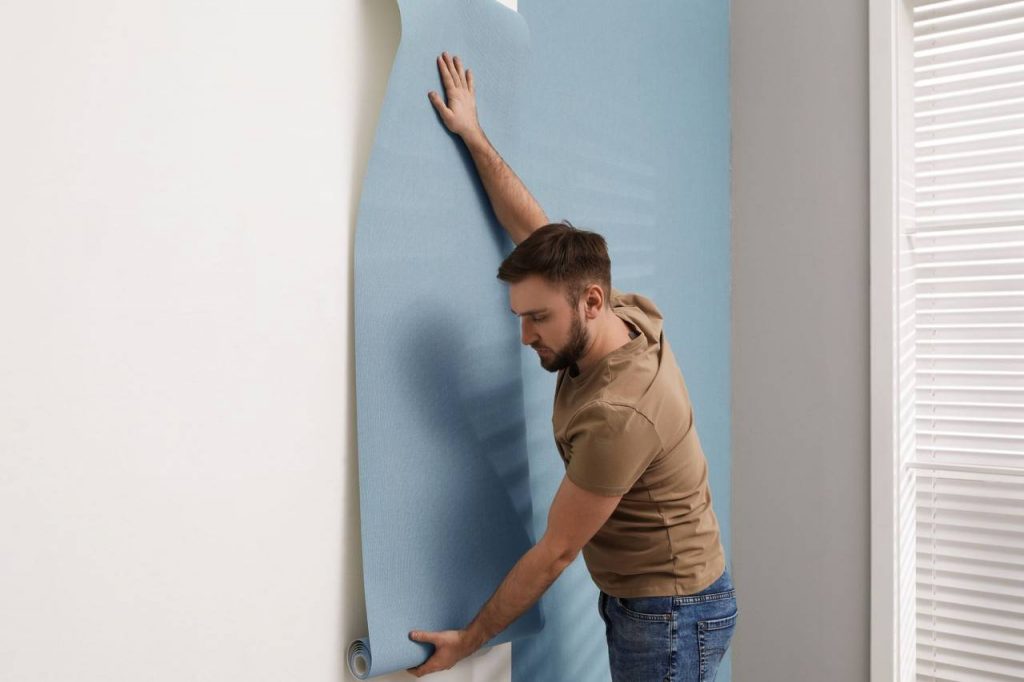 Homem realizando instalação de papel de parede na cor azul em parede branca