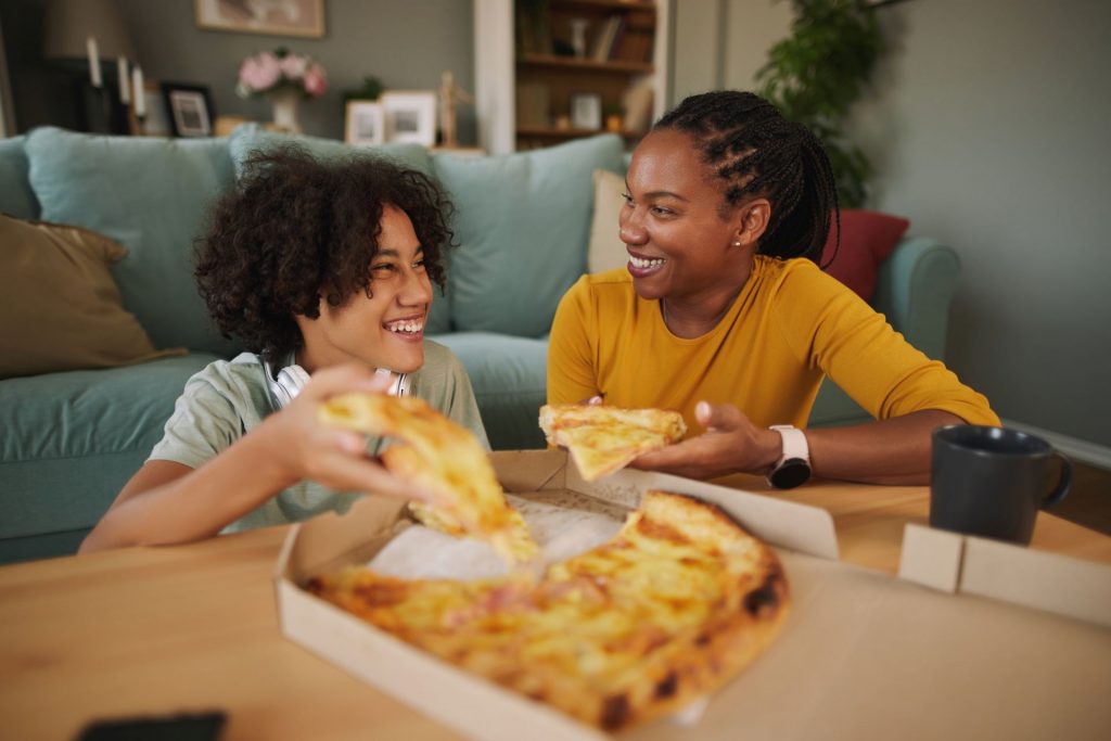 mãe e filho comendo pizza na sala de casa celebrando o dia das mães