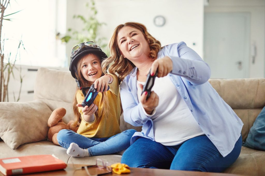 mãe e filha sentadas no sofá da sala jogando videogame no dia das mães