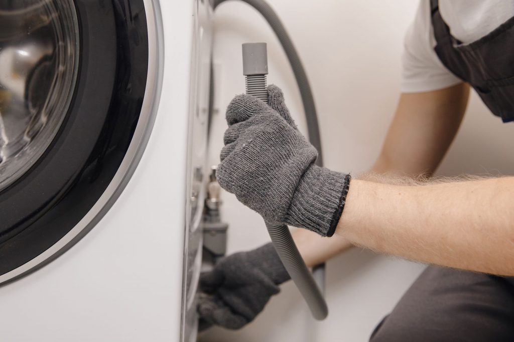 Homem verificando as tubulações da máquina de lavar roupas durante de limpeza de eletrodomésticos