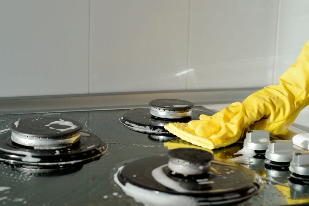 Pessoa com luvas de limpeza, limpando com uma esponja a parte superior do fogão tipo cooktop