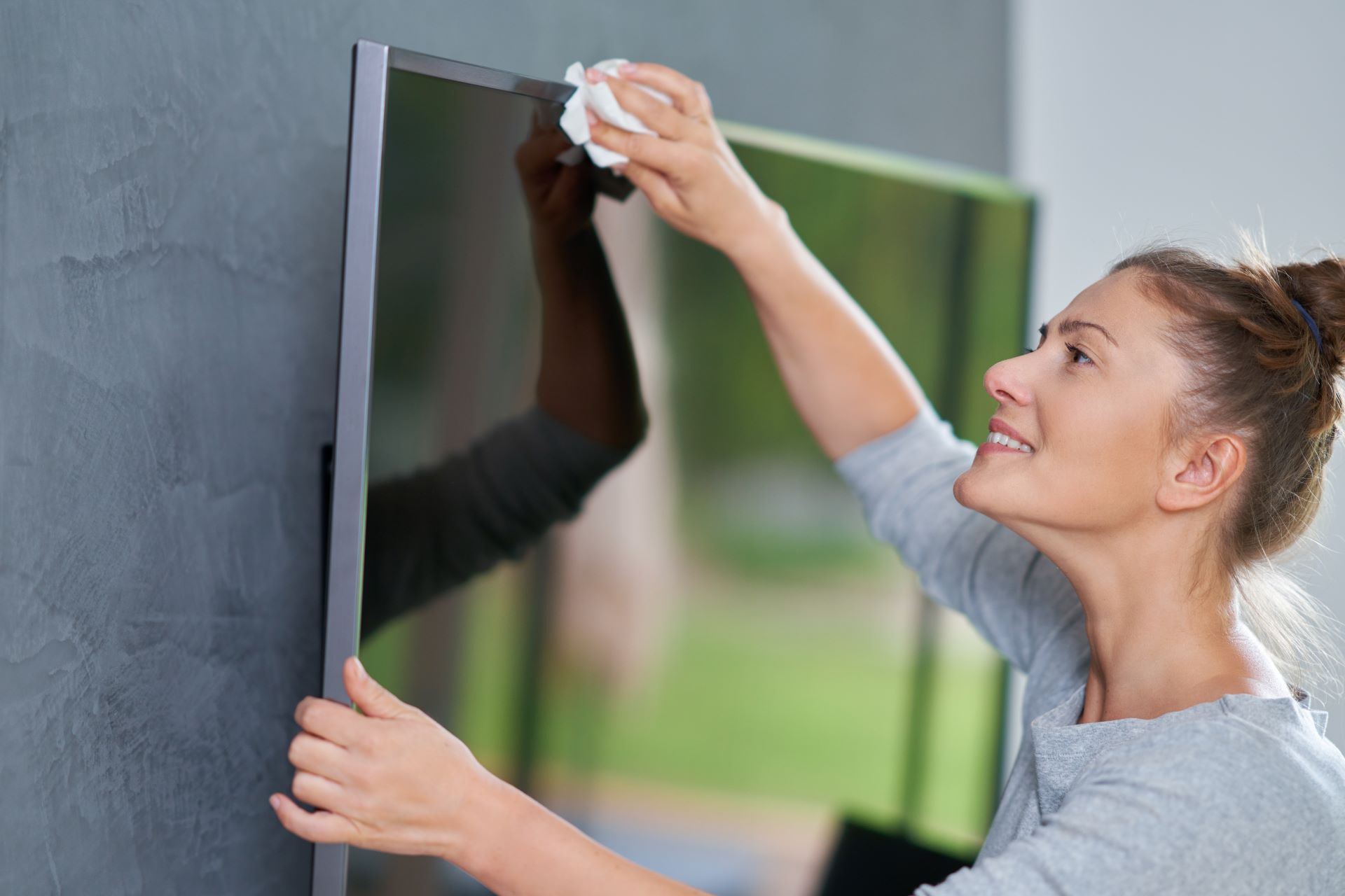 Mulher limpando a parte externa da smart tv com um pano de limpeza de eletrodomésticos