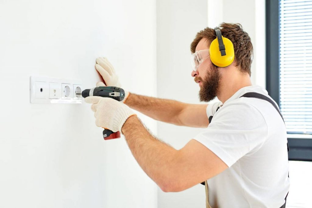 Homem furando uma parede com furadeira e proteção de ouvido apresentando o que é epi