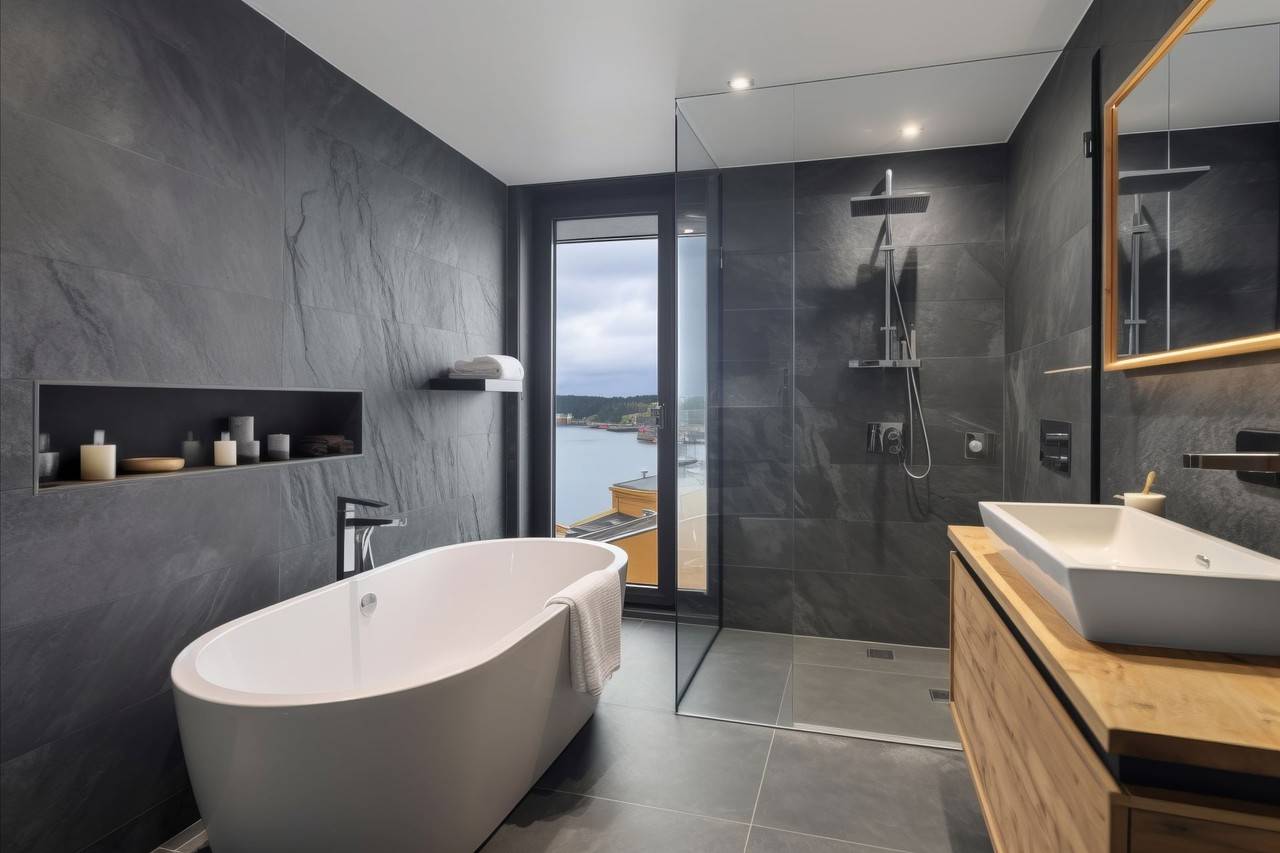Banheiro com revestimento em paredes no tom cinza, banheira de cor branca e box de vidro