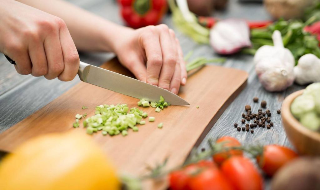 Pessoa picando legume em tábua de madeira, utensílio de cozinha